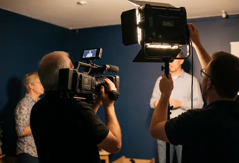 Vidéaste en action utilisant une caméra de cinéma et une lumière LED dans un environnement de travail réaliste adapté aux entreprises
