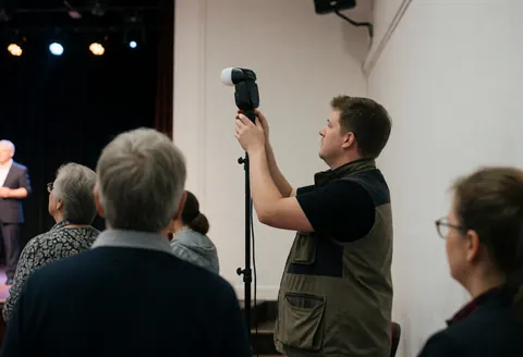 Un photographe professionnel ajuste son équipement de flash sur une scène avec des lumières et un public en arrière-plan.