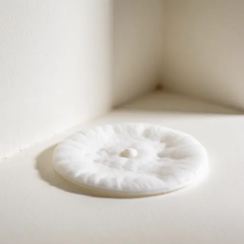 Détail d'une lingette en coton blanc présentant un petit point noir dans un coin intérieur, évoquant les soins de la peau et l'hygiène.