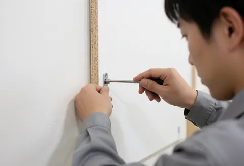 Un technicien ajuste un verrou à came sur un panneau de particules blanches à l'aide d'une clé hexagonale, dans un environnement de travail professionnel avec un fond blanc.