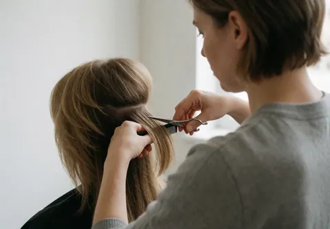 Un coiffeur professionnel coupe les cheveux d'un client dans un salon lumineux aux murs blancs, utilisant des ciseaux pour un service de coiffure.