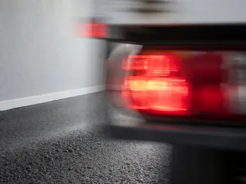 Détails des feux arrière rouges d'un camion en mouvement sur l'asphalté avec des murs gris clair, effet de flou de mouvement, idéal pour un photographe cinétique.