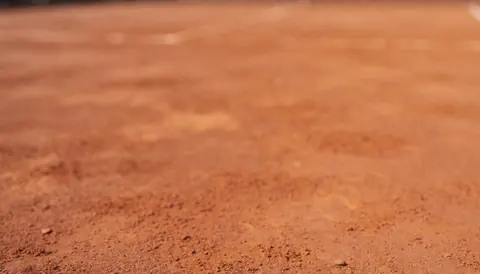 Arrière-plan flou d'un court de tennis en terre battue avec texture rougeâtre et lumière naturelle, idéal pour textes de services sportifs