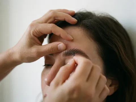 Un professionnel applique minutieusement un produit sur les sourcils d'un client à l'aide d'un pinceau, dans le cadre d'un service de beauté en cours.