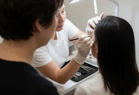 Application précise de pigment pour le lissage des sourcils en salon de beauté avec outils spécialisés et éclairage professionnel.