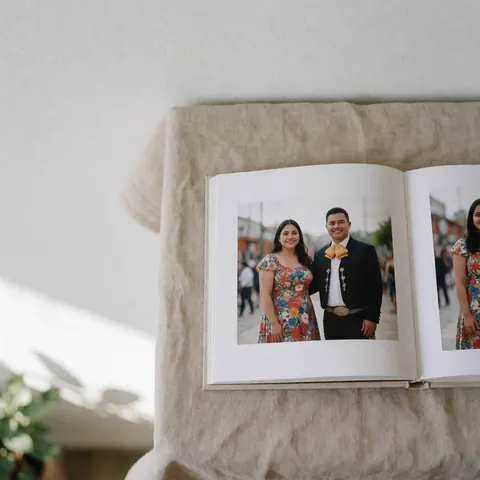 Album de photos ouvert montrant un couple vêtu d'une tenue traditionnelle charro sur un tissu beige éclairé par la lumière naturelle.