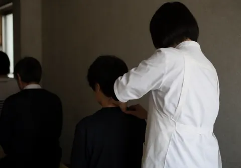 Un masseur professionnel réalise un massage thaïlandais sur la nuque d'un client assis dans un espace calme aux murs en béton et à l'éclairage doux.