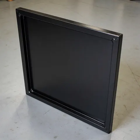 Panneau métallique réparé avec peinture noire mate, joints soudés visibles sur sol en béton dans un atelier de métallerie.