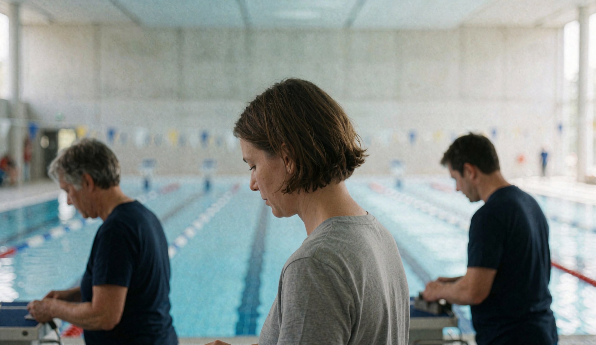 Des entraîneurs de natation travaillent dans une piscine olympique avec des nageurs, des murs en béton et de l'eau bleue.