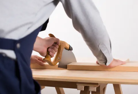 Un ouvrier utilise une scie électrique pour couper une planche de bois dans un atelier de menuiserie, illustrant le travail en cours.