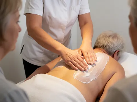 Un thérapeute en uniforme blanc applique de l'huile sur le dos nu d'un client dans une salle claire aux murs lisses, dans le cadre d'un massage suédois.