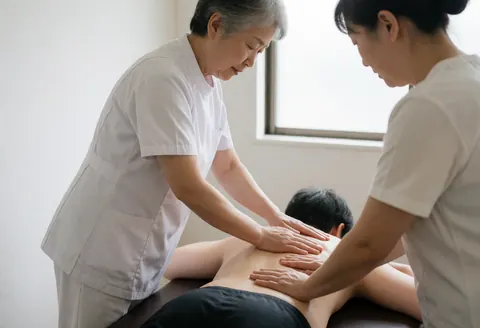 Deux professionnels réalisent un massage suédois sur le dos d'un client allongé sur une table dans un salon aux murs blancs.