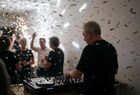 Un dj professionnel mixe de la musique lors d'une fête avec du confetti doré et des lumières brillantes sur fond de murs blancs.