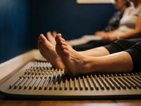Des pieds reposant sur un tapis de réflexologie avec une texture en relief, dans une salle de traitement aux murs bleus.