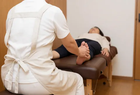 Un thérapeute réalise un massage des pieds d'un client allongé sur une table de massage dans un cadre chaleureux et professionnel.