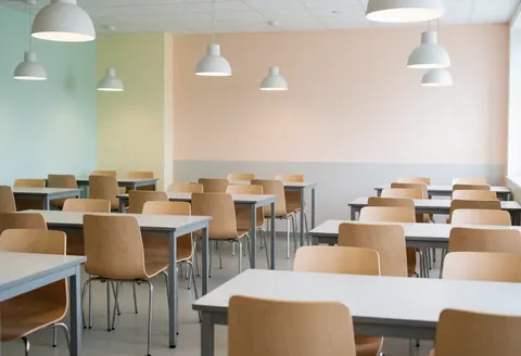Cafétéria universitaire moderne avec tables et chaises vides, murs pastel et lumières suspendues, ambiance propre et accueillante