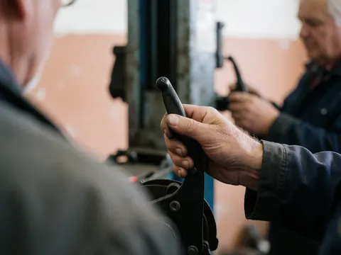 Une main d'un mécanicien tient une manette de frein dans un atelier de vélos avec des murs en plâtre et un éclairage doux.