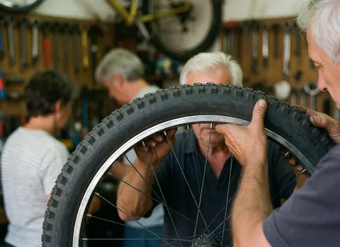 Un mécanicien en train d'installer un pneu sur une roue de vélo dans un atelier avec des outils visibles en arrière-plan.