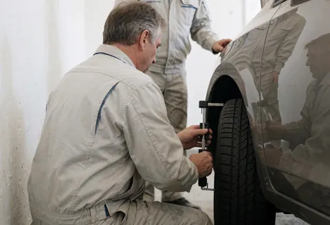 Mécanicien professionnel utilisant un jauge de profondeur de bande de roulement pour inspecter un pneu dans un atelier automobile aux murs blancs.