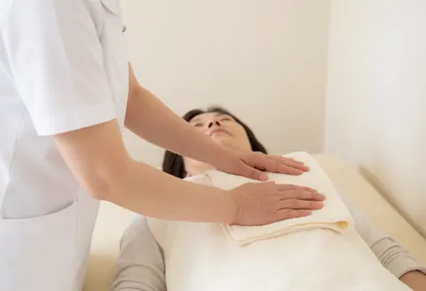 Un thérapeute en uniforme blanc place une serviette sur le torse d'une cliente allongée sur une table de massage dans un cadre relaxant.