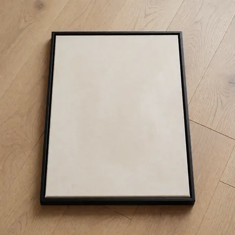 Un cadre noir fin contenant une œuvre d'art abstraite posé sur un sol en bois clair, prêt à être expédié.
