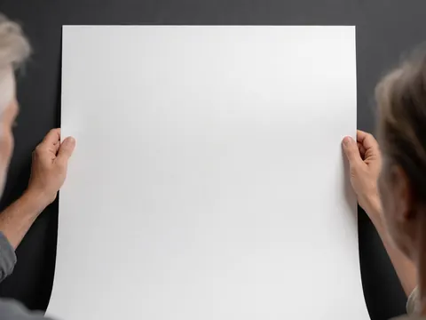 Deux mains tiennent une feuille blanche sur un mur gris, idéal pour la conception et la présentation de produits.