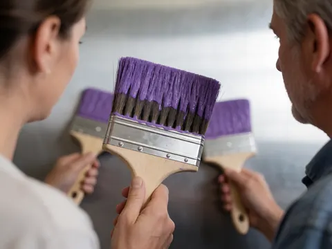 Deux personnes tenant des pinceaux de peinture violets, travaillant sur un mur gris, scène de peinture professionnelle.