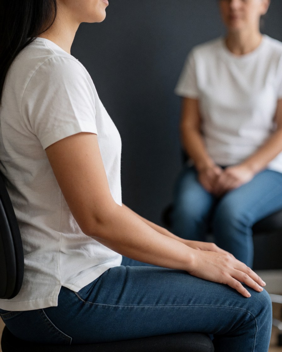 Un client est assis sur une chaise dans un bureau, adoptant une posture relaxée. Les murs gris et la lumière naturelle créent une ambiance calme et professionnelle.
