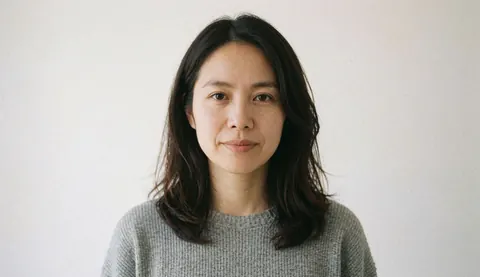 Portrait d'une femme souriante portant un pull gris, regardant l'objectif devant un fond blanc uni pour un usage professionnel.