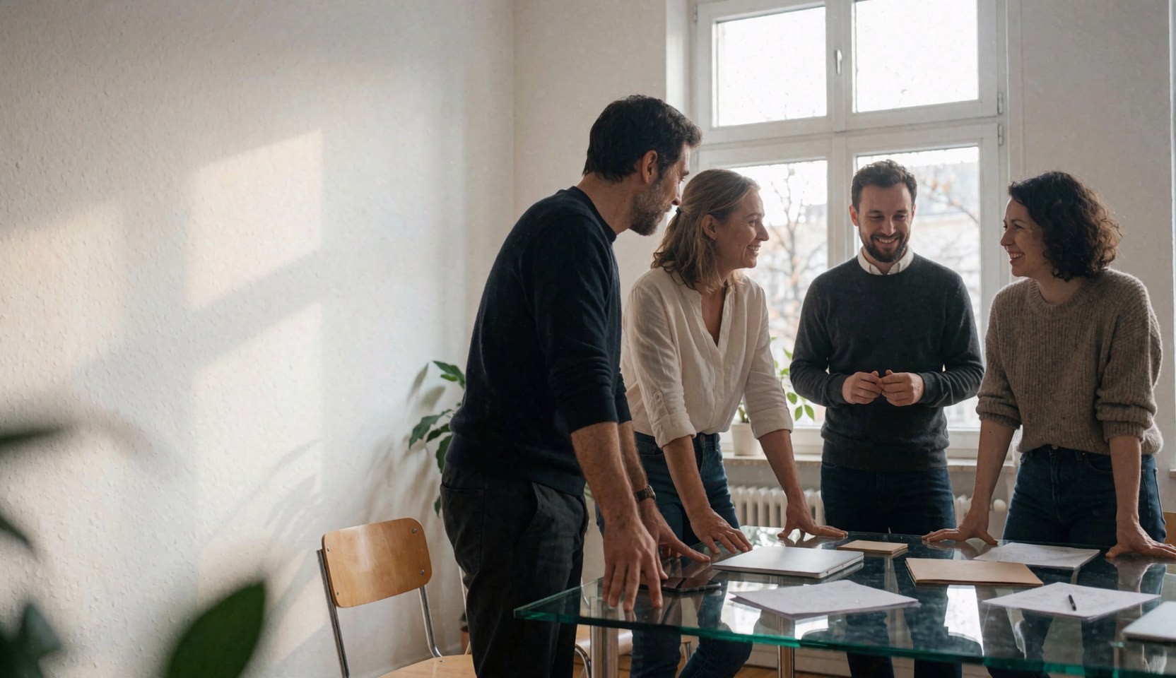 Quatre professionnels dans un bureau moderne avec table en verre et lumière naturelle, travaillant ensemble dans un environnement professionnel.