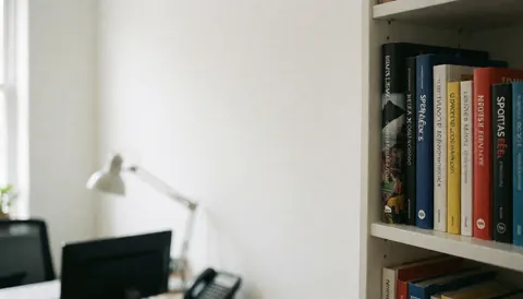 Étagère contenant des ouvrages sur les sciences du sport, placée dans un bureau aux murs blancs et à la lumière naturelle, servant de fond pour un texte lié au cyclisme.