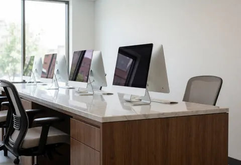 Un bureau en marbre blanc équipé de plusieurs écrans d'ordinateur et de chaises, installé dans un intérieur lumineux et contemporain.