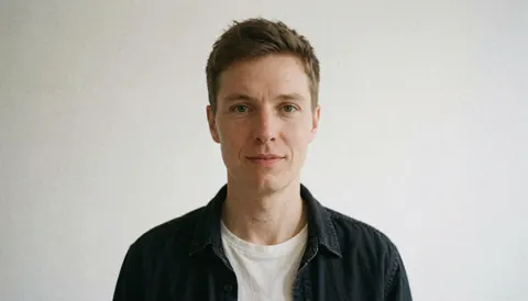 Portrait d'un homme en chemise foncée sur t-shirt blanc regardant l'objectif sur fond neutre pour usage professionnel.