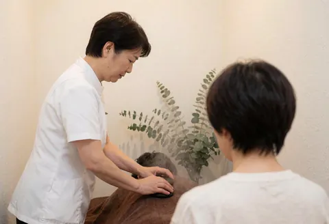 Un thérapeute en uniforme blanc effectue un massage aux pierres chaudes sur le dos d'un client dans un spa calme aux murs blancs.