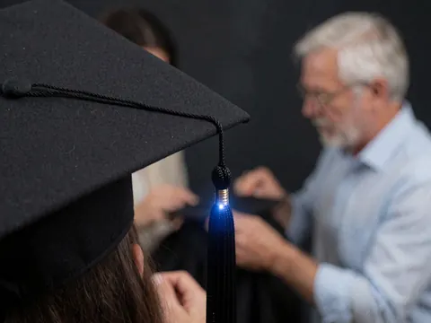 Gros plan d'une main ajustant la grenouillère d'une casquette de diplômé sur fond sombre avec éclairage bleu, détail professionnel pour photographe de cérémonies.