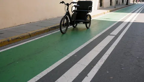 Un tricycle électrique à trois roues est garé sur une voie verte urbaine avec des marquages au sol blancs et gris, adapté aux services de transport en ville.