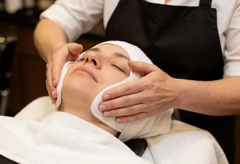 Des mains professionnelles posent un masque à la vapeur sur le visage d'une cliente dans un salon de massage.