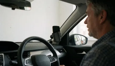 Intérieur de véhicule montrant un smartphone maintenu par un support magnétique sur la grille d'aération, avec le volant visible et un fond clair, illustrant les accessoires automobiles.