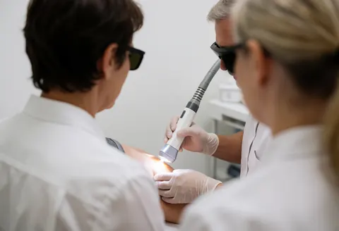 Un technicien portant des lunettes de protection applique un traitement au laser sur la peau d'un client dans un centre d'esthétique.