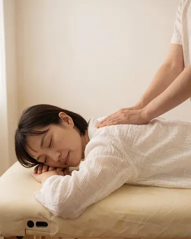 Une cliente se repose sur une table de massage tandis qu'une praticienne lui applique un massage thaïlandé dans un cadre relaxant aux murs blancs.