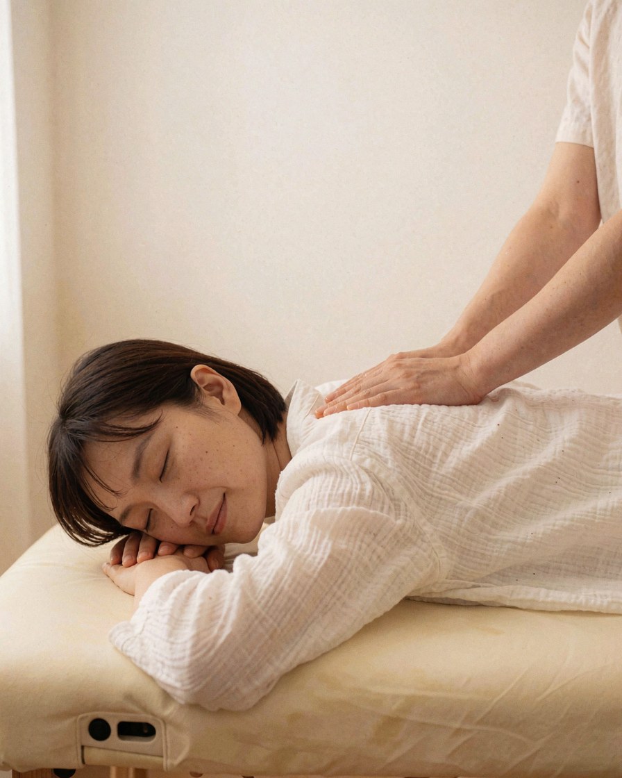 Une cliente se repose sur une table de massage tandis qu'une praticienne lui applique un massage thaïlandé dans un cadre relaxant aux murs blancs.
