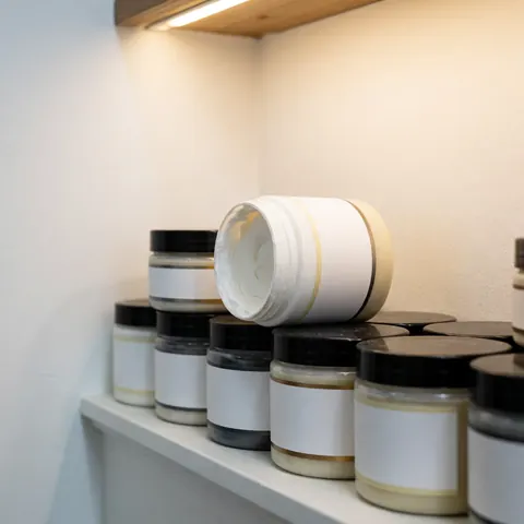 Des bocaux contenant une pâte blanche sont disposés sur une étagère devant un mur blanc, sous un éclairage chaleureux, dans un atelier automobile.