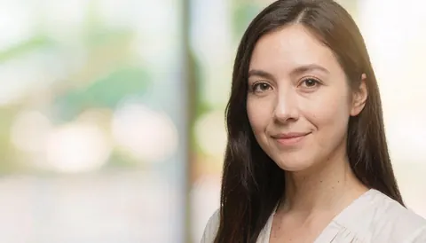 Portrait d'une femme souriante portant une chemise blanche avec un arrière-plan flou aux lumières douces, adapté au contexte professionnel.