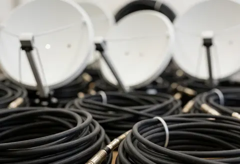 Des antennes paraboliques blanches et des câbles coaxiaux enroulés dans un entrepôt, illustrant les équipements pour l'installation d'antennes.