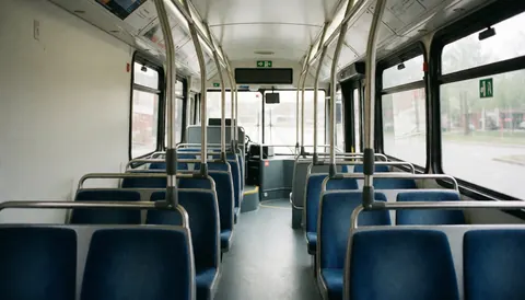 Vue intérieure d'un bus de transport public montrant des rangées de sièges bleus, des barres métalliques, de grandes fenêtres et un sol propre et vide.