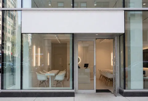 Façade moderne d'un salon de manucure avec portes vitrées et tables blanches visibles depuis l'extérieur.