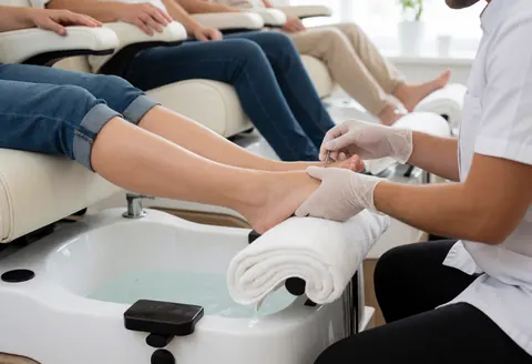 Manuciste avec des gants travaillant sur les pieds dans un bain de pédicure, environnement propre et professionnel, idéal pour un salon de beauté.