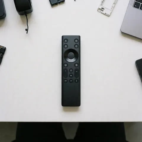 Télécommande universelle noire posée sur une table blanche propre, entourée de composants électroniques et d'un ordinateur portable, idéale pour la réparation de téléviseurs.