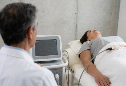 Un thérapeute observe l'écran d'un appareil pendant qu'une patiente reçoit un traitement d'électrothérapie dans une clinique.