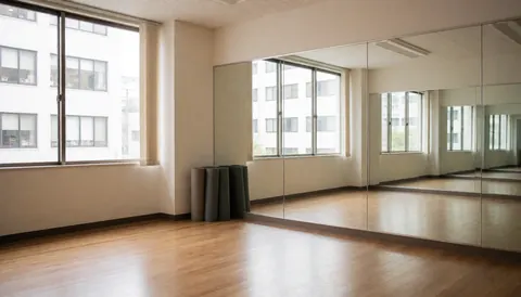 Studio de danse vide avec sol en bois, miroirs muraux et tapis roulés dans un coin, idéal pour les cours de danse.